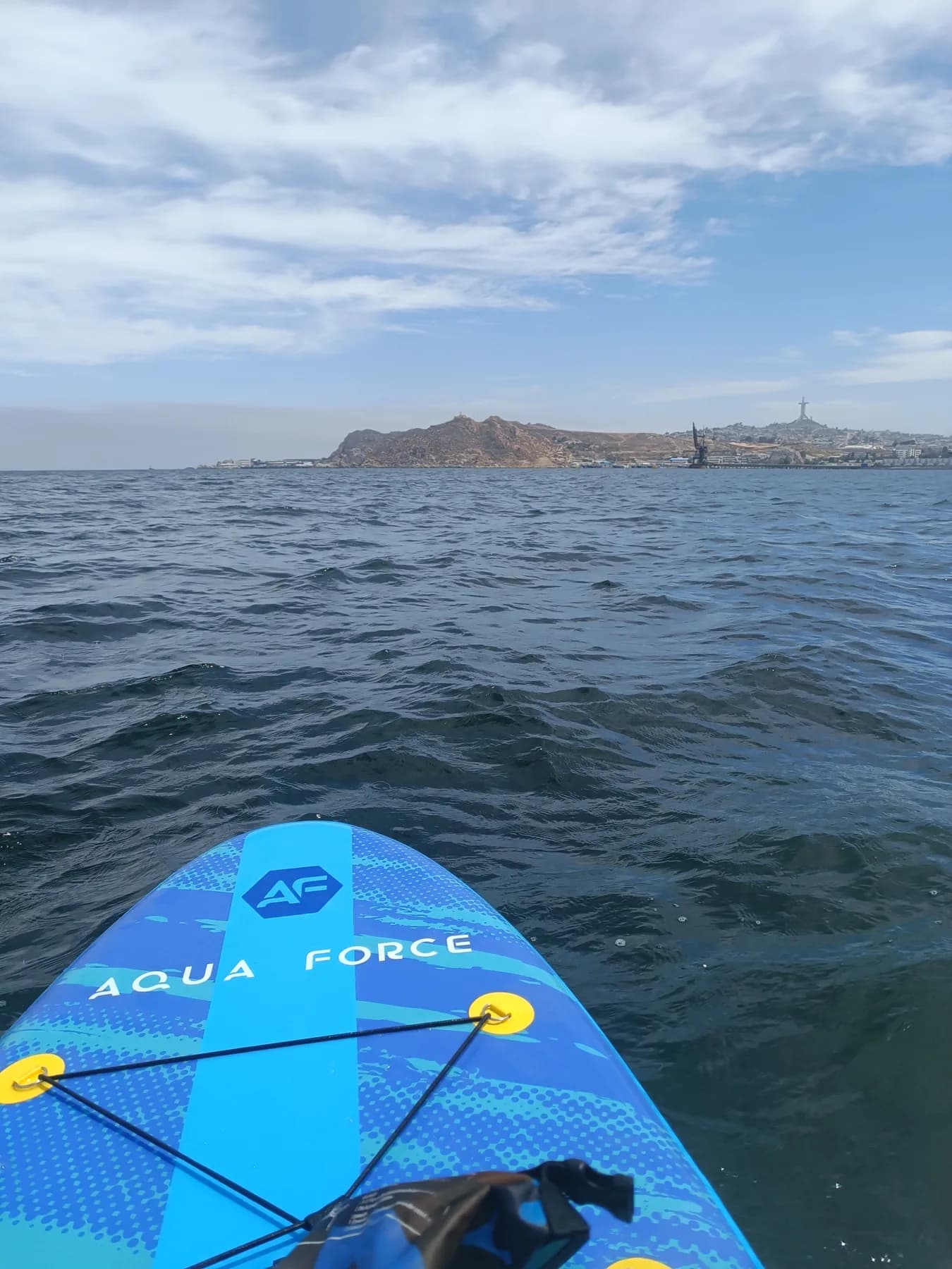 Una tabla de SUP en la bahía de La Herradura, con la Cruz del Tercer Milenio al fondo